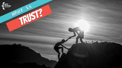 One person helping another climb up a large rock