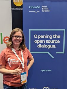 Felicity Brand tanding in front of a conference banner, "Opening the open source dialogue"